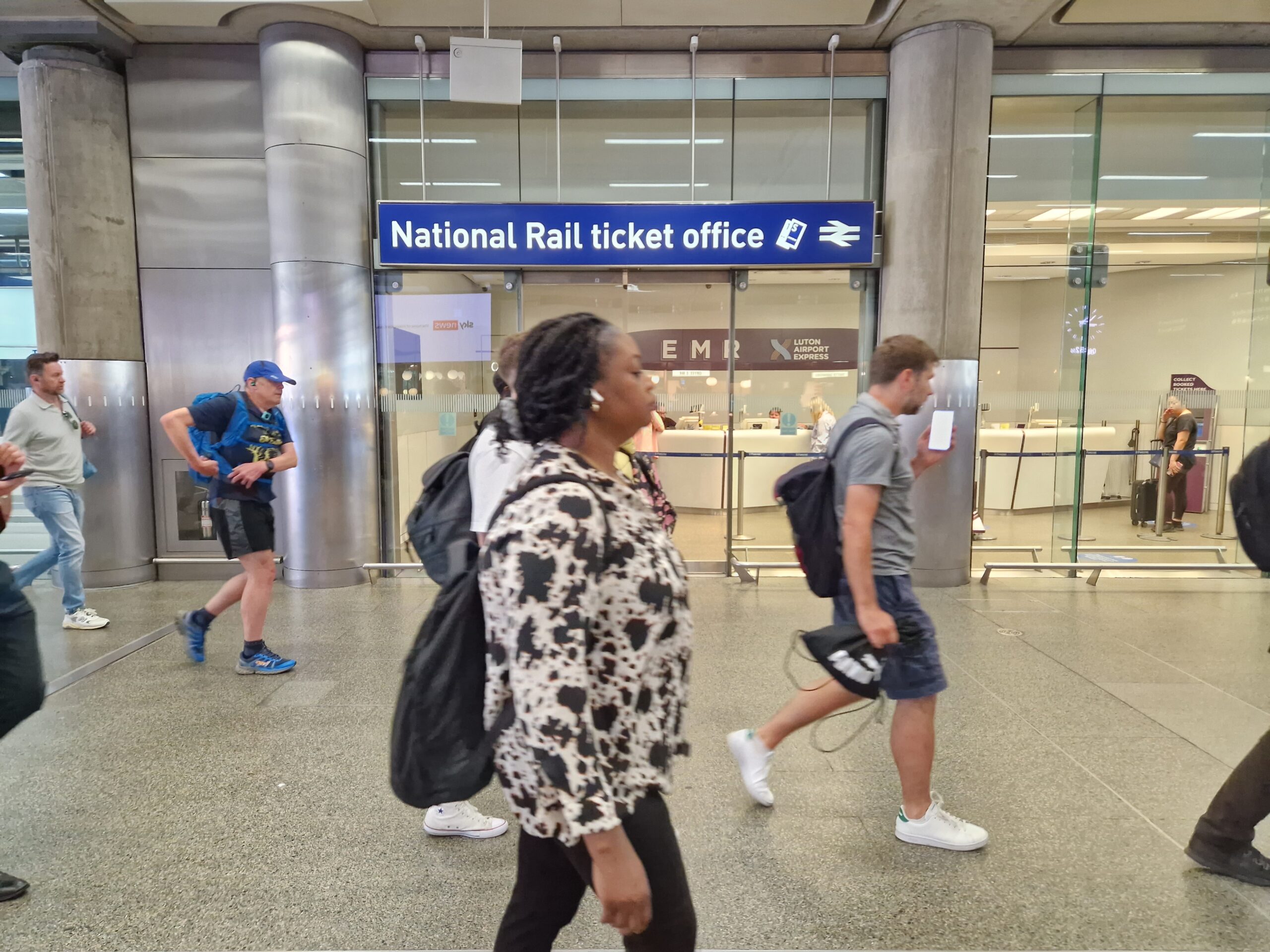 Passengers at a train station walking past a National Rail ticket office.