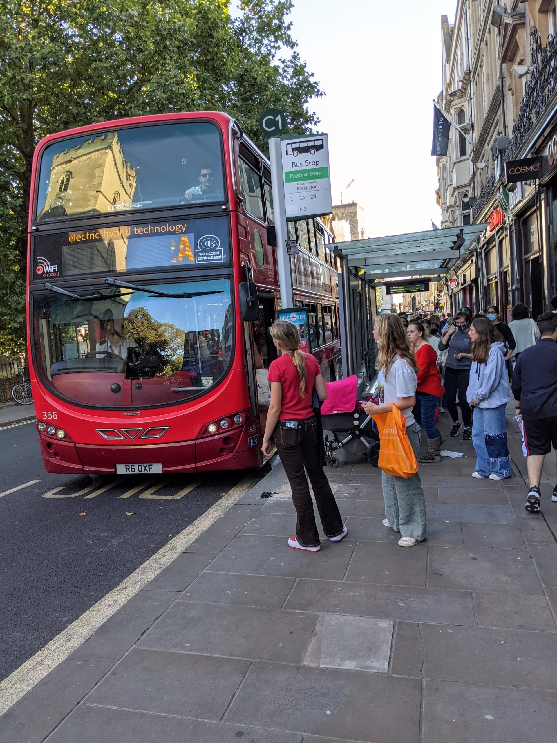 young people standing at bus stop with red bus waiting